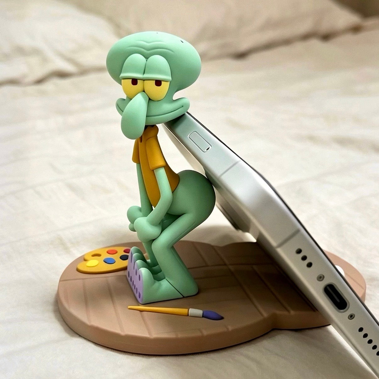 Squidward figurine with a paint palette and brush on a phone stand