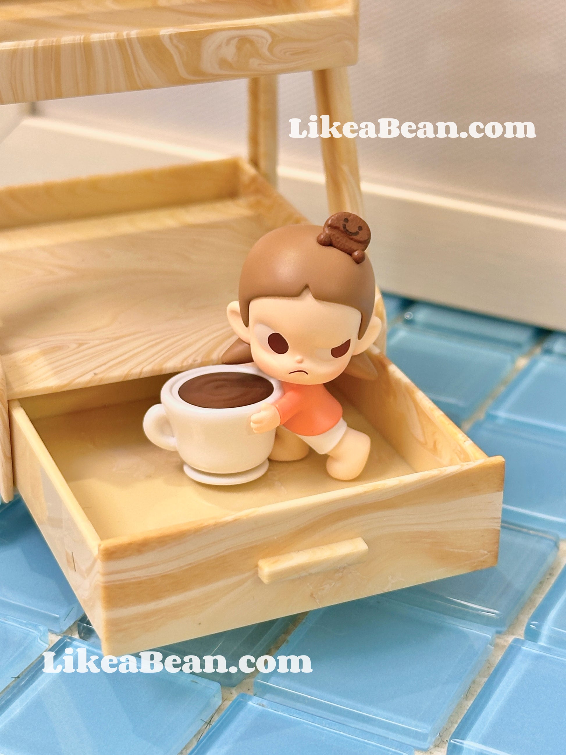 Small figurine of a child with a cup on a wooden shelf, with 'LikeaBean.com' branding.